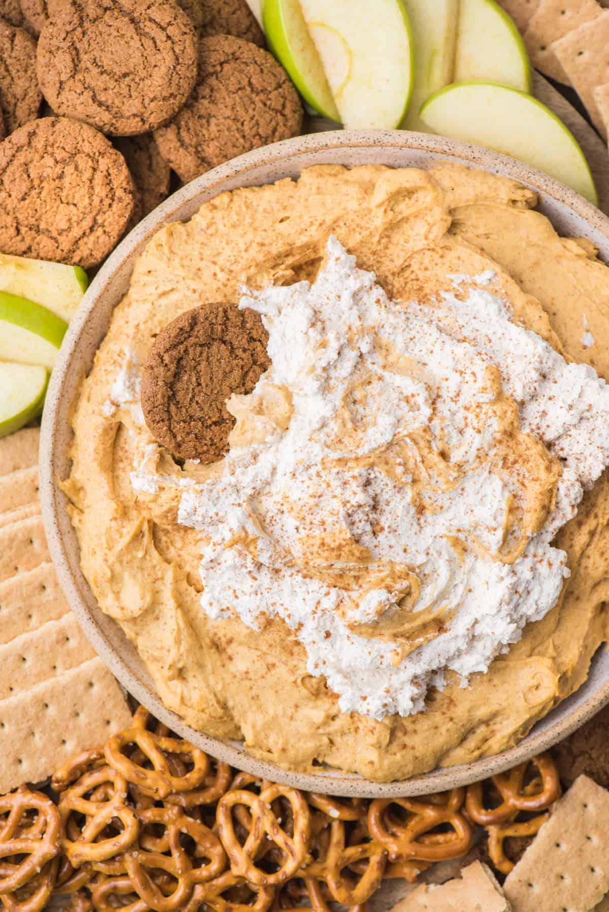 **Mousse di Zucca** 7 Cremosa crema di zucca con panna montata in una ciotola, circondata da pretzel, biscotti allo zenzero, cracker Graham e fette di mela verde su un piatto di legno.