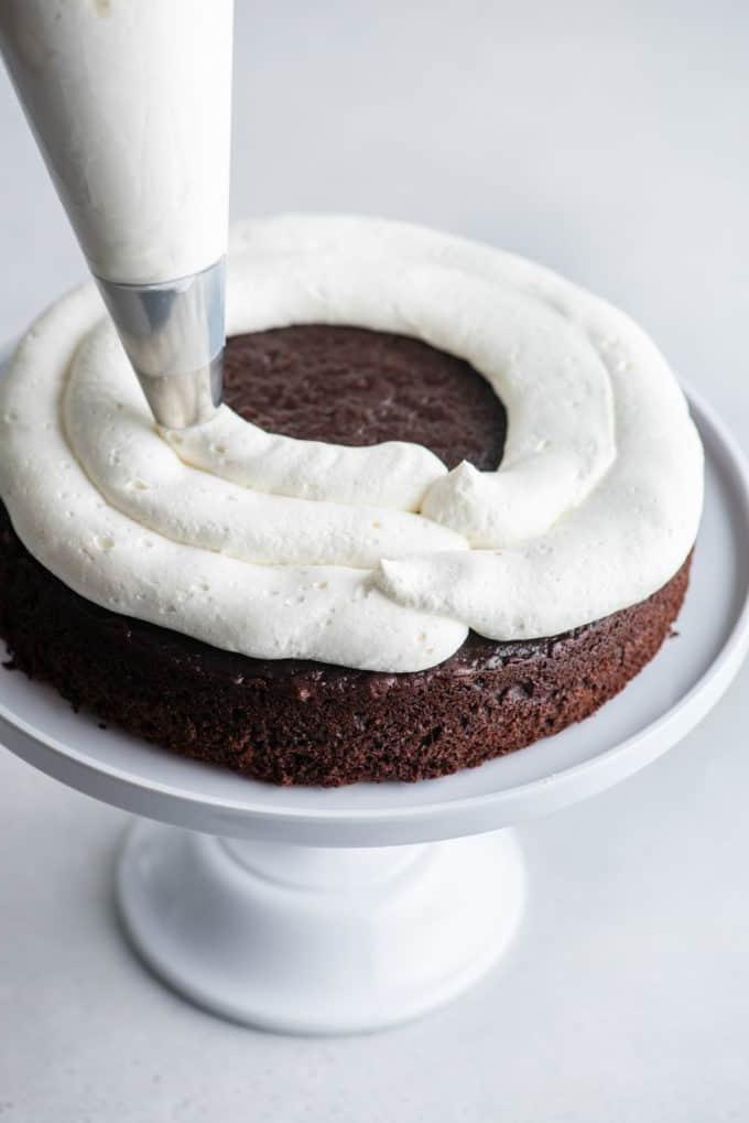 Torta Foresta Nera 7 Uno strato di pan di Spagna al cioccolato su un'alzatina bianca con la panna montata stabilizzata che viene messa sopra con una sac à poche