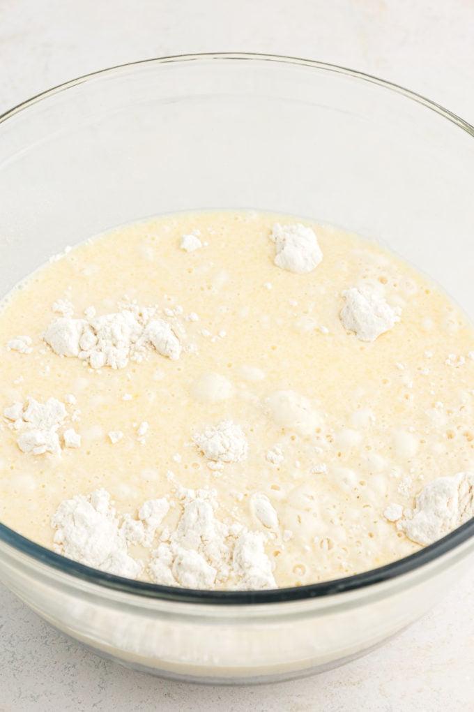 Ricetta Pancakes in Teglia 7 Ingredienti per l'impasto dei pancake al forno in teglia in una ciotola di vetro trasparente su una superficie bianca.