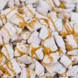 **Dolcetti Croccanti al Cioccolato Bianco di Capodanno** 8 A plate of new years eve puppy chow, coated in powdered sugar, drizzled with gold-colored icing, and topped with small gold star-shaped sprinkles.