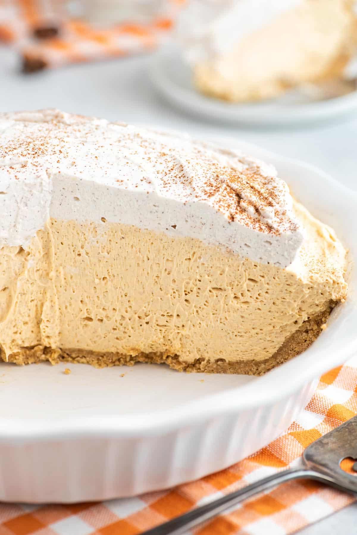 Questa torta di zucca senza cottura, veloce e facile, è leggera e cremosa - una deliziosa variante della classica torta di zucca. Un pezzo leggero e cremoso di torta di zucca senza cottura adagiato su un piatto da dessert bianco.
