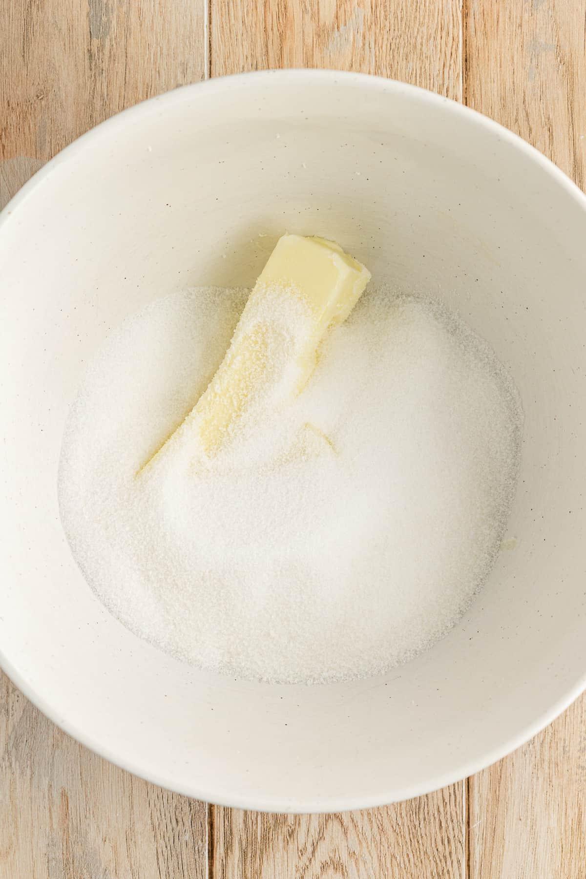Ricetta Facile Torta alla Banana 8 Una ciotola bianca su una superficie di legno con zucchero semolato e un pezzo di burro