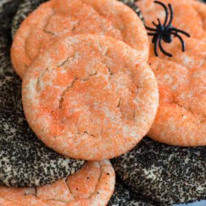 Semplici Biscotti di Zucchero di Halloween 8 Un piatto di biscotti di zucchero di Halloween ricoperti di zuccherini arancioni e neri, disposti in un mucchio festivo, sormontati da un piccolo ragno di plastica nero per decorazione.