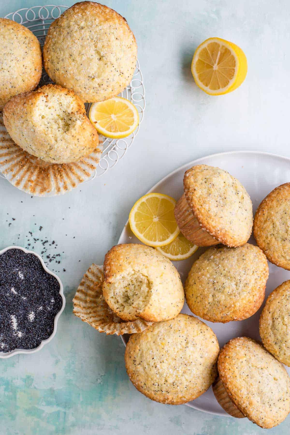 Migliori Muffin al Limone e Semi di Papavero 8 due piatti di muffin al limone e semi di papavero impilati, alcuni parzialmente mangiati, disposti con fette di limone e una ciotola di semi di papavero
