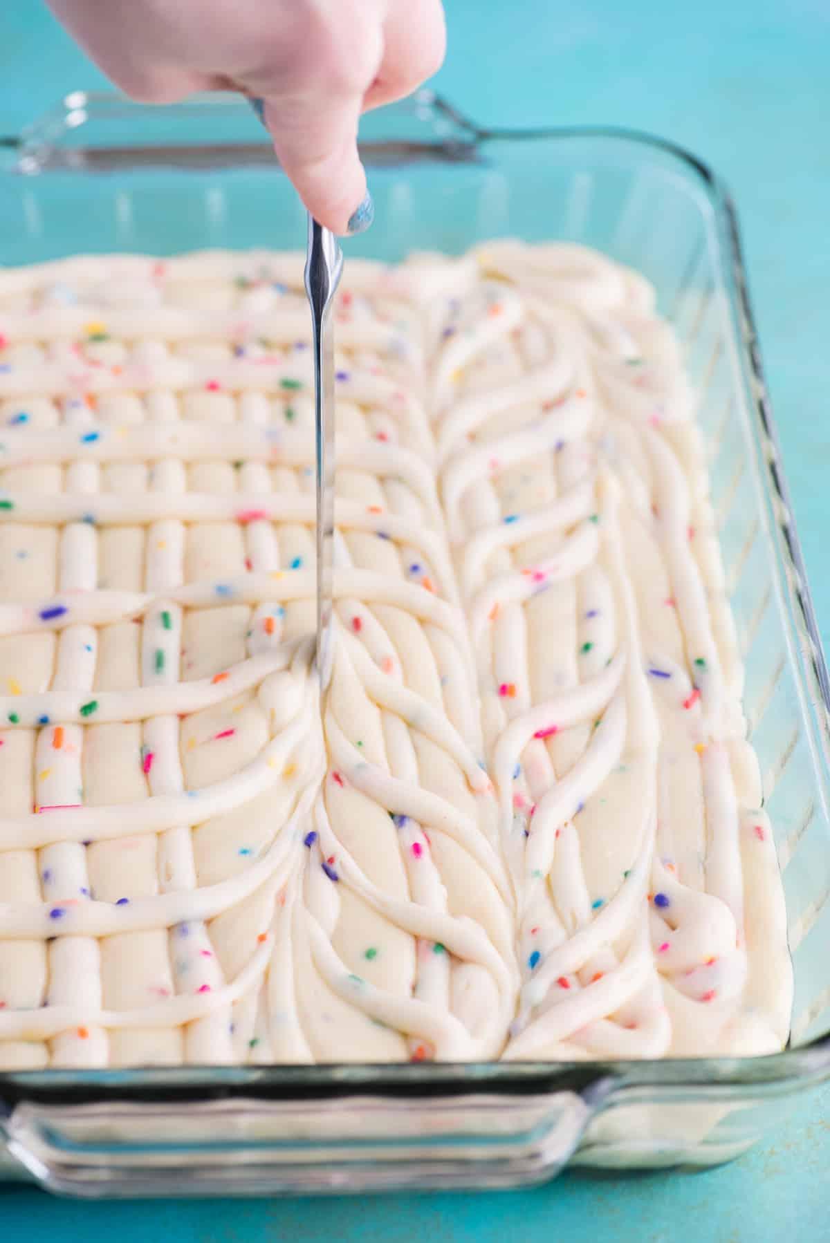 Questa torta terremoto funfetti è un mix per torta bianca arricchito con zuccherini e gocce di cioccolato funfetti. Lo strato di glassa al formaggio cremoso si fonde nella torta creando crepe e fessure in superficie. #earthquakecake #funfetticake #cake Mescolando l'impasto della torta e la glassa al formaggio cremoso con un coltello da burro in una teglia di vetro 9x13 pollici