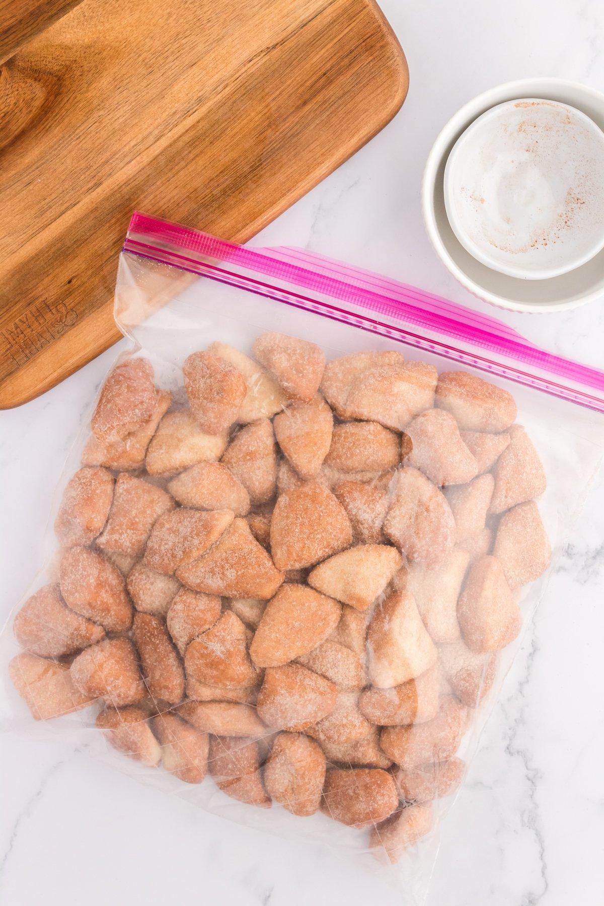 Pane delle scimmie di biscotti 9 Una busta di plastica da un gallone piena di pezzi di impasto di biscotti mescolati con zucchero alla cannella, accanto a due ciotole vuote e un tagliere di legno