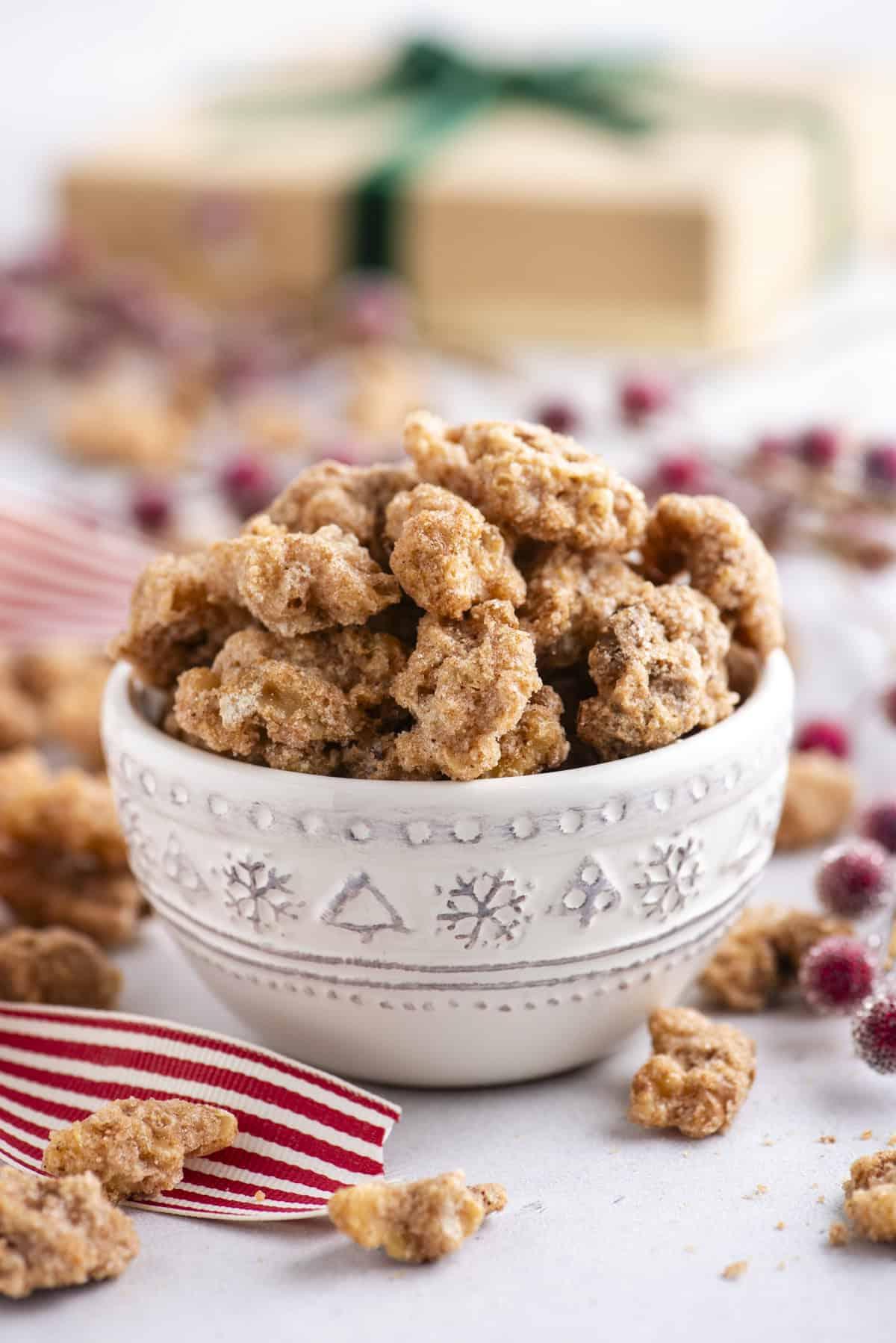 noci pralinate in una piccola ciotola bianca con più sparse e un nastro a strisce rosse e bianche
