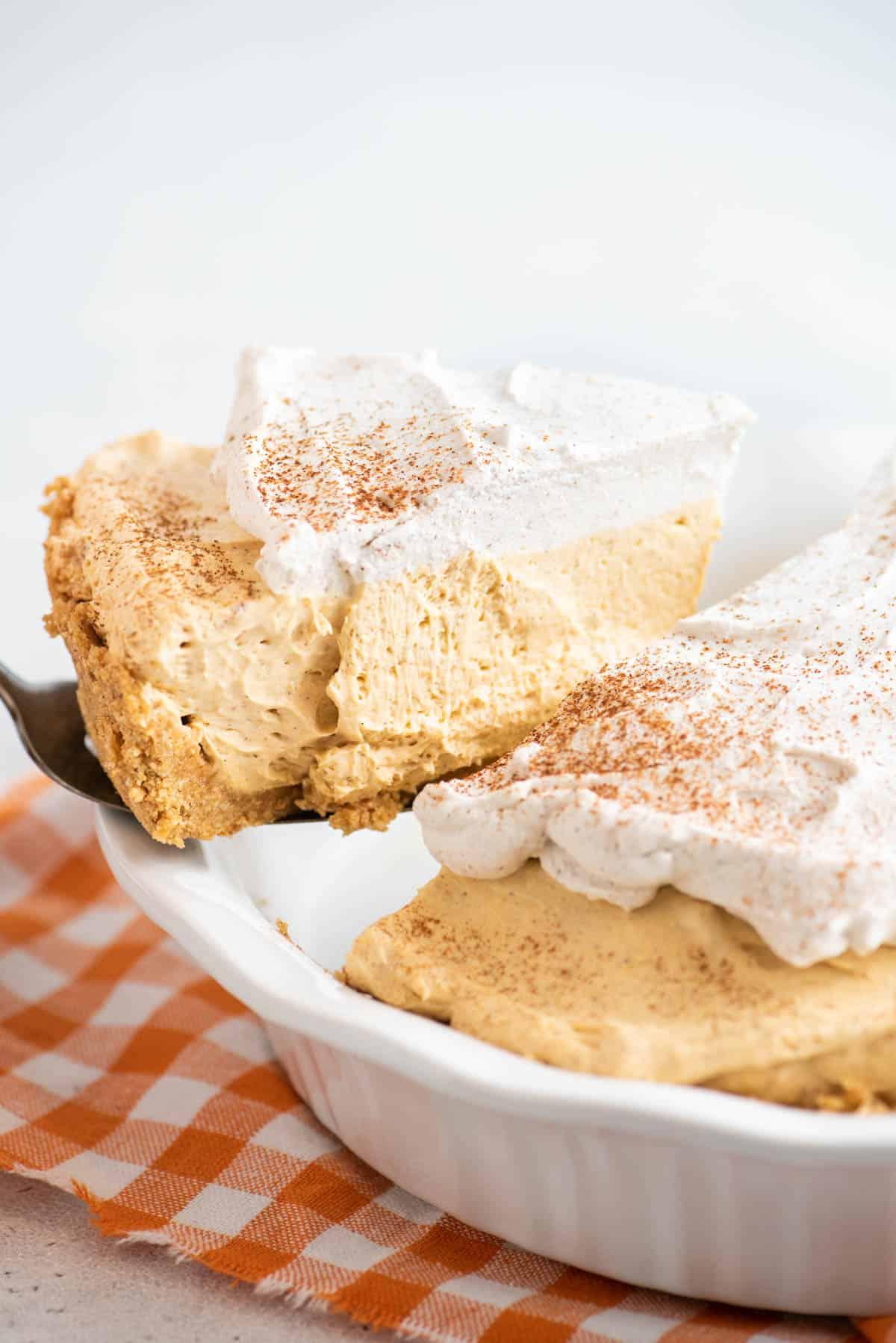 Questa torta di zucca senza cottura, veloce e facile, è leggera e cremosa - una deliziosa variante della classica torta di zucca. Una fetta di torta di zucca senza cottura viene servita dalla teglia.