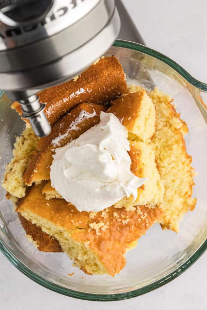 torta spezzettata in pezzi grandi con una grande cucchiaiata di glassa bianca sopra, all'interno di una ciotola di una planetaria