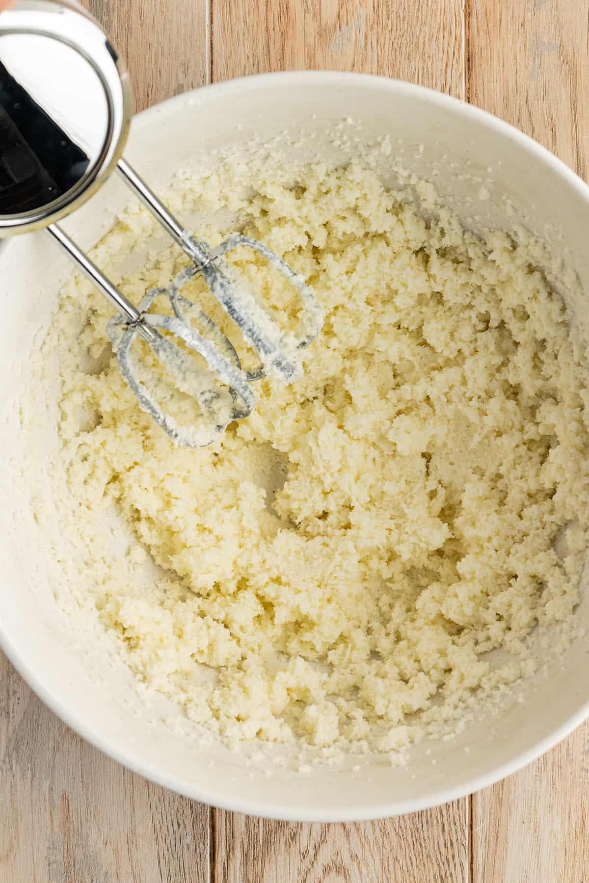 Ricetta Facile Torta alla Banana 9 Una ciotola bianca su una superficie di legno con burro e zucchero mescolati insieme da un mixer elettrico appoggiato all'interno della ciotola