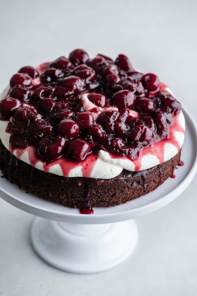 Torta Foresta Nera 9 Uno strato di pan di Spagna al cioccolato su un'alzatina bianca con la panna montata stabilizzata sopra e una salsa di ciliegie sopra, con un altro strato di pan di Spagna al cioccolato sopra
