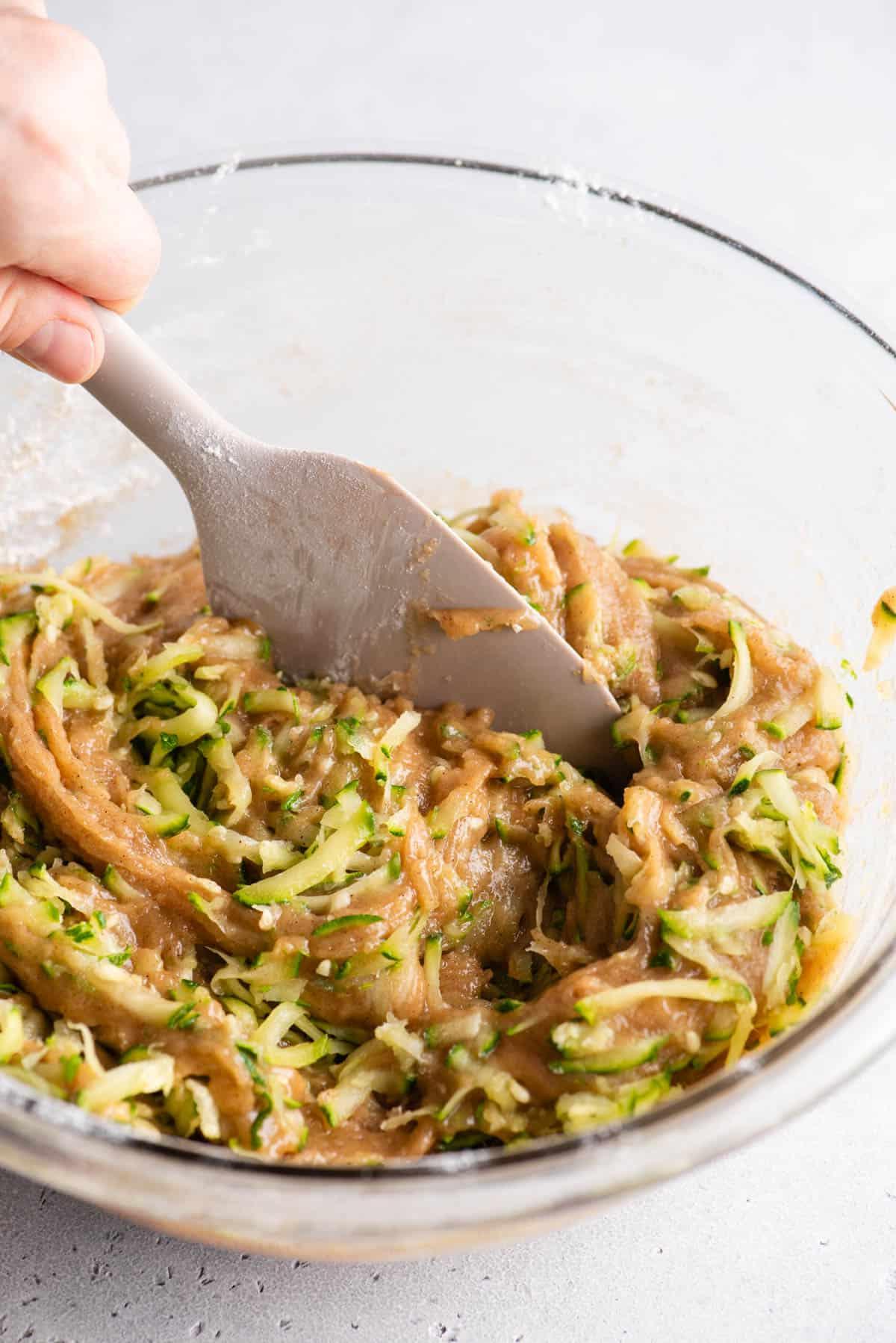 Migliori Muffin alle Zucchine 9 Una ciotola di vetro trasparente con impasto per muffin di zucchine e zucchine grattugiate mescolate insieme con una spatola