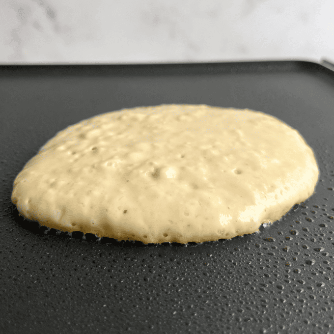 Pancakes Soffici Fatti in Casa 10 Un pancake che cuoce su una piastra e non è ancora stato girato, con bolle che iniziano a formarsi sulla superficie.