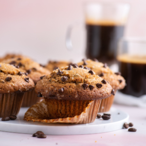 muffin al cappuccino con gocce di cioccolato su un piatto bianco con gocce di cioccolato sparse intorno e due tazze di cappuccino sullo sfondo