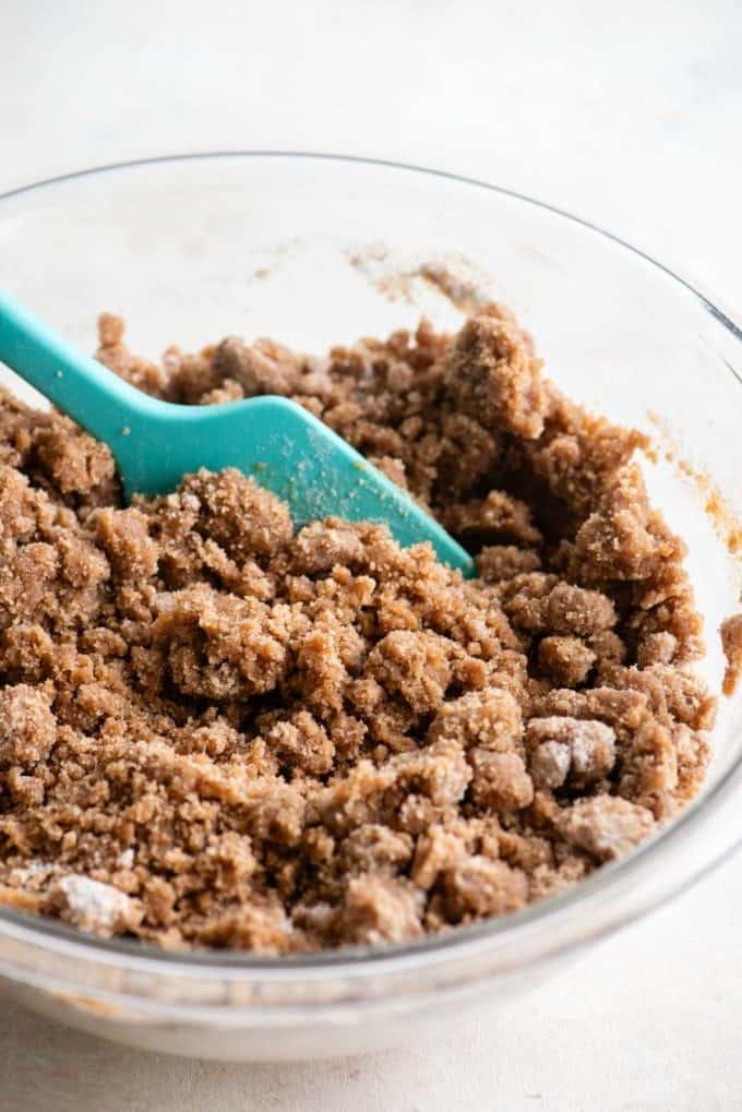 Ricetta Torta Umida al Caffè 10 Primo piano del topping di crumble per torta al caffè in una ciotola di vetro trasparente con una spatola verde acqua al suo interno