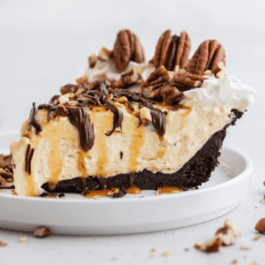 Torta di Tartaruga 10 Una fetta di Torta Tartaruga guarnita con noci pecan, gocce di cioccolato e caramello, su un piccolo piatto bianco con pezzi di noci pecan sparsi intorno.