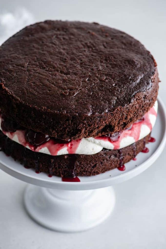 Torta Foresta Nera 10 Uno strato di pan di Spagna al cioccolato su un'alzatina bianca con la panna montata stabilizzata sopra e una salsa di ciliegie sopra, con un altro strato di pan di Spagna al cioccolato sopra