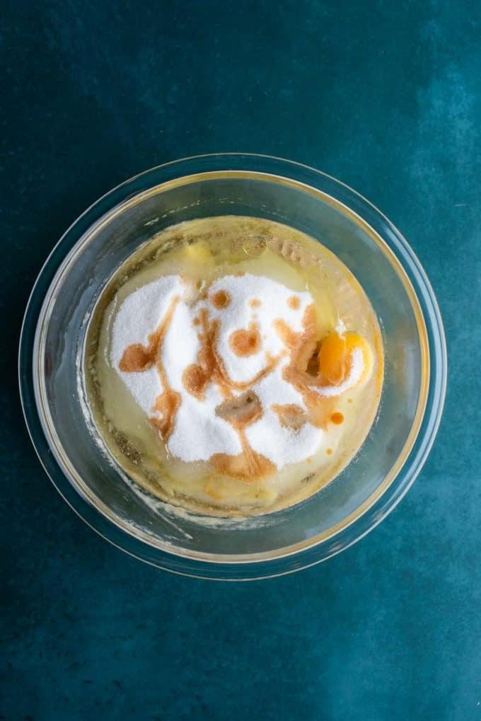 Il Miglior Pan di Banane con Gocce di Cioccolato 10 Ingredienti liquidi per il pane alle banane e gocce di cioccolato in una ciotola di vetro trasparente su una superficie color ottanio scuro, tra cui banane schiacciate, olio vegetale, uova, zucchero semolato ed estratto di vaniglia.