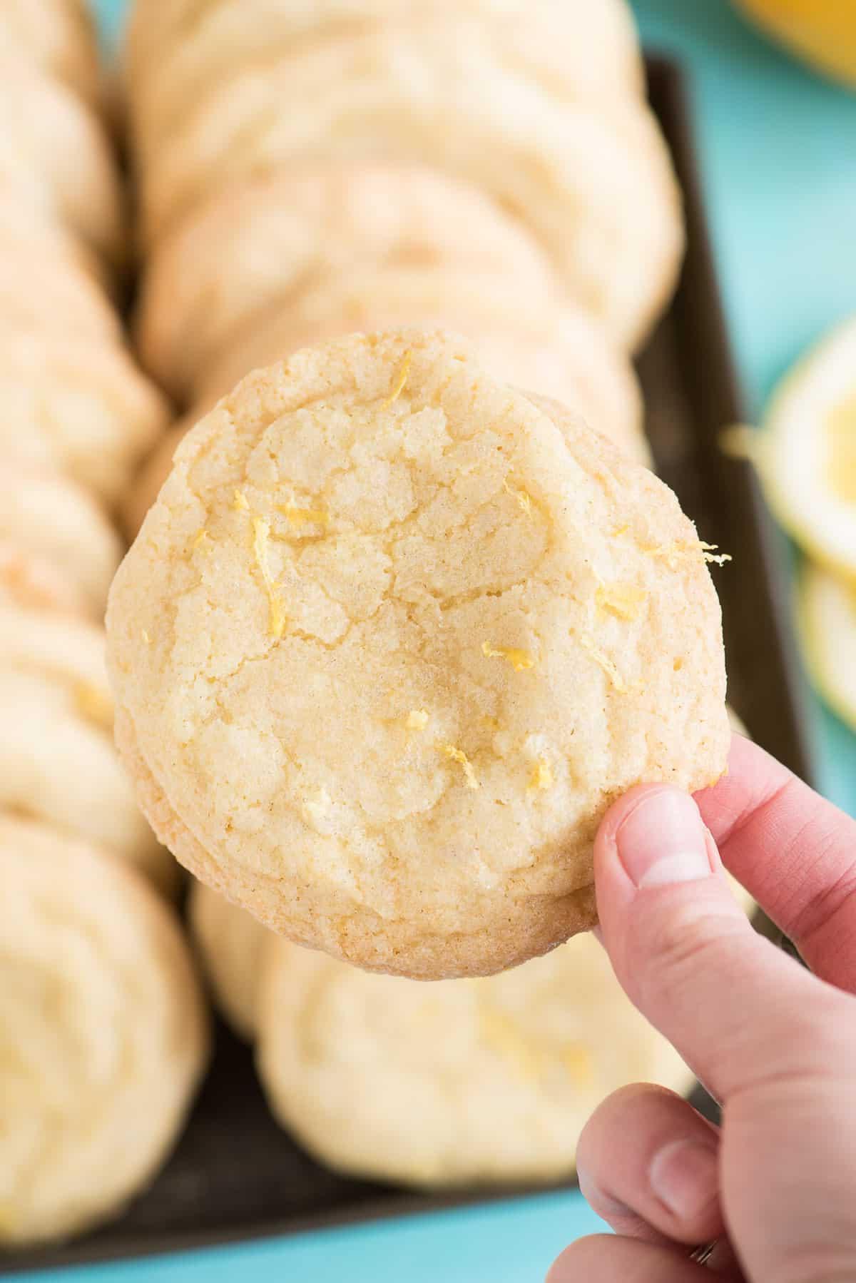 Biscotti al limone ricoperti di zucchero - un dolce estivo agrumato! Mano che tiene un biscotto al limone con altri biscotti sullo sfondo
