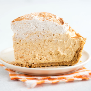 Torta di Zucca con Panna Montata Senza Cottura 2 Un pezzo leggero e cremoso di torta di zucca senza cottura adagiato su un piatto da dessert, sopra un tovagliolo a quadretti arancioni.
