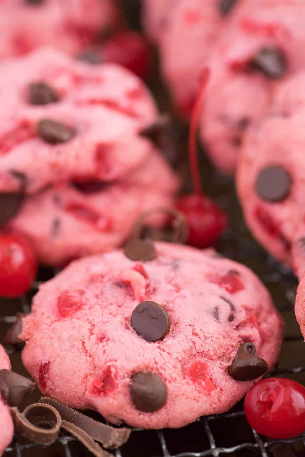 Ricetta di biscotti alle ciliegie maraschino spessi e masticabili! Ricetta di biscotti alle ciliegie candite. biscotti rosa alle ciliegie maraschino e gocce di cioccolato su teglia con ciliegie e gocce di cioccolato