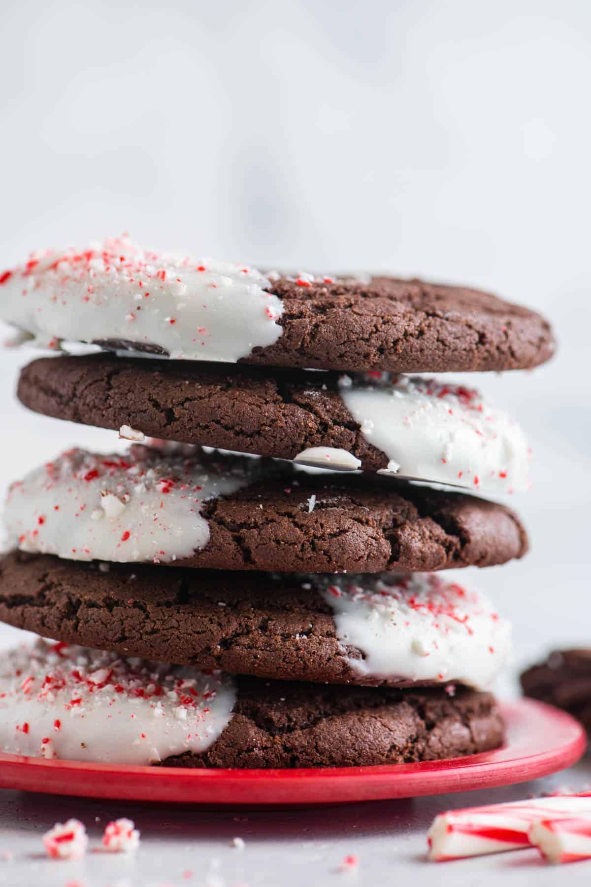 Questi Biscotti al Cioccolato e Bastoncini di Zucchero sono morbidi, gommosi, immersi nel cioccolato bianco e cosparsi di bastoncini di zucchero tritati. Una pila di biscotti al cioccolato e bastoncini di zucchero