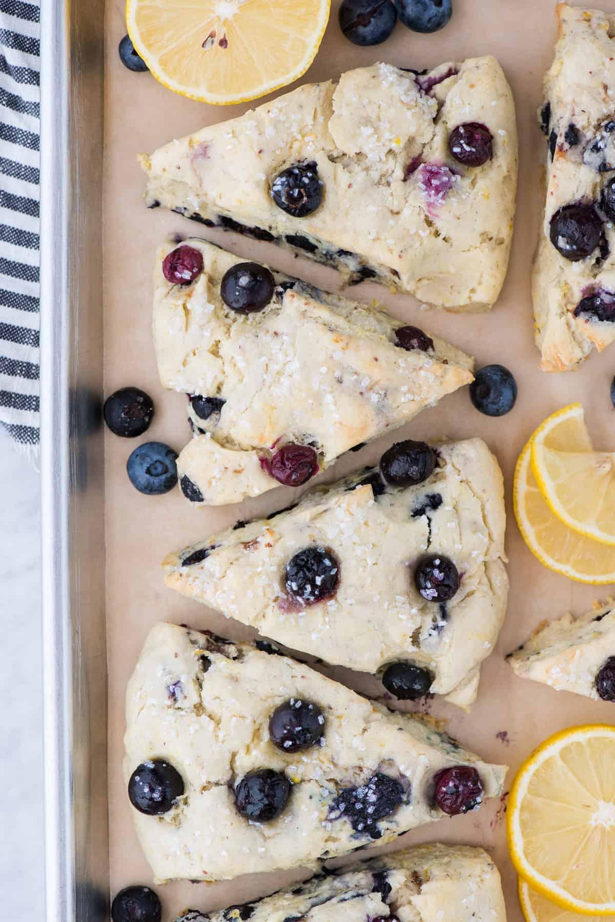 I Migliori Scones al Limone e Mirtilli 2 Scones al limone e mirtilli su carta forno marrone con fette di limone e mirtilli