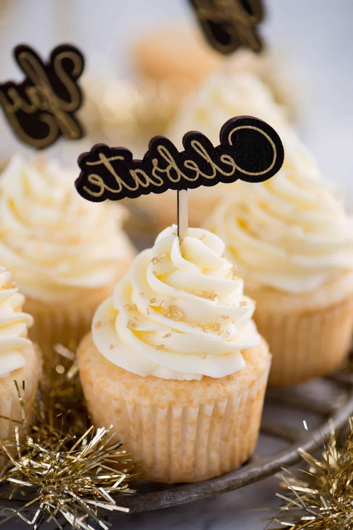 Cupcakes Facili allo Champagne 2 Facili cupcakes allo champagne con glassa al burro e champagne, decorati con zuccherini dorati e un topper per cupcake con la scritta "celebrate"