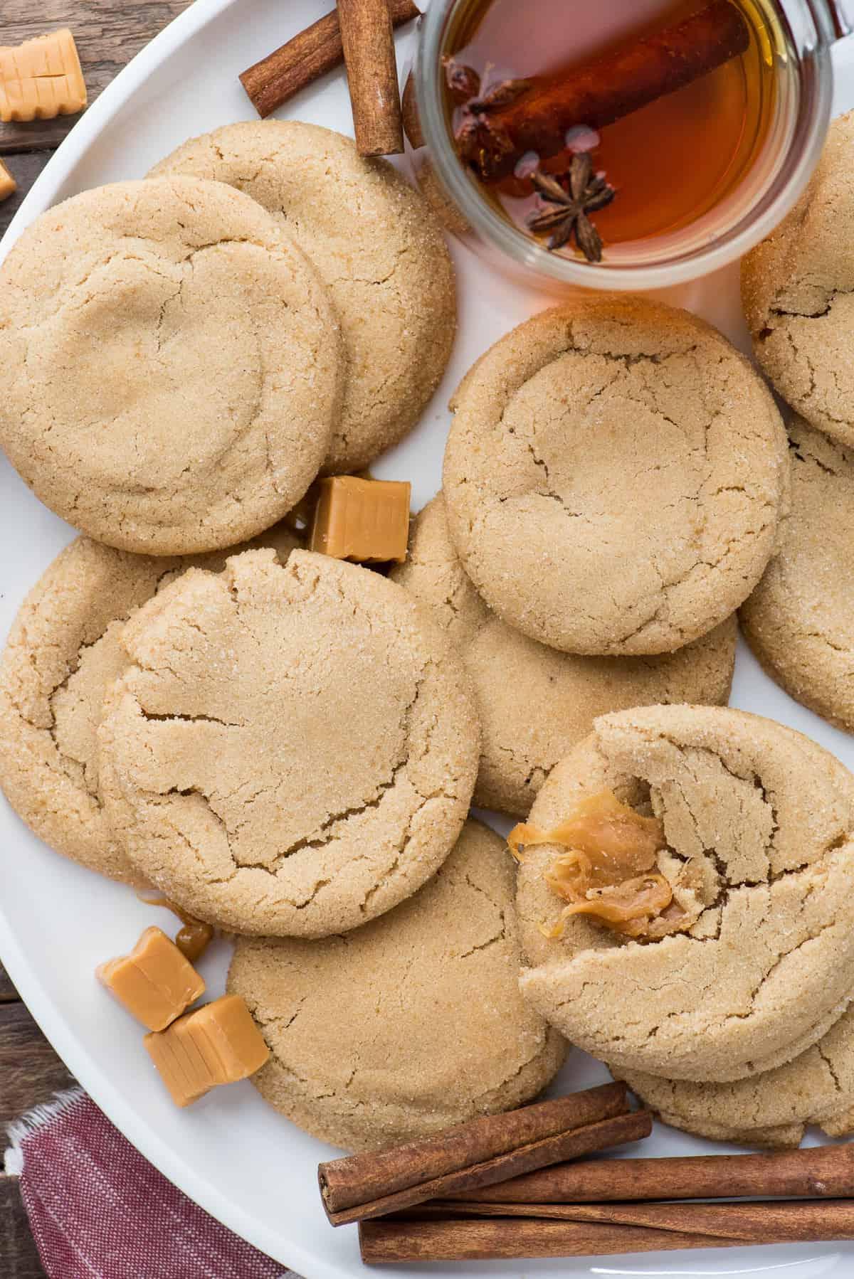 Biscotti alle Mele e al Caramello 2 apple cookies with caramel center on white round platter with caramel squares and cinnamon sticks