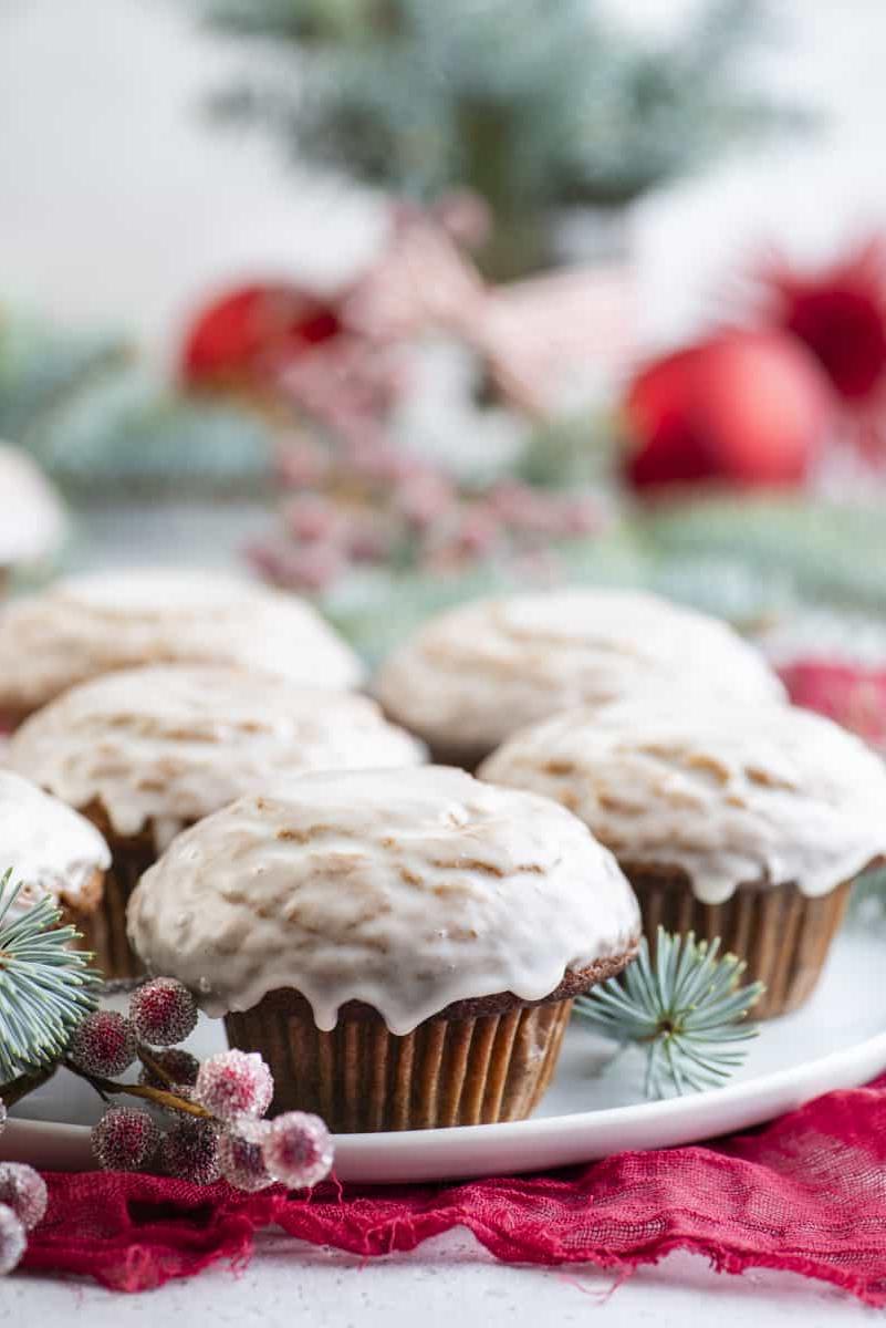 Muffin al pan di zenzero 2 Muffin al pan di zenzero con glassa alla vaniglia disposti su un piatto bianco con bacche rosse zuccherate e rami di abete sempreverdi