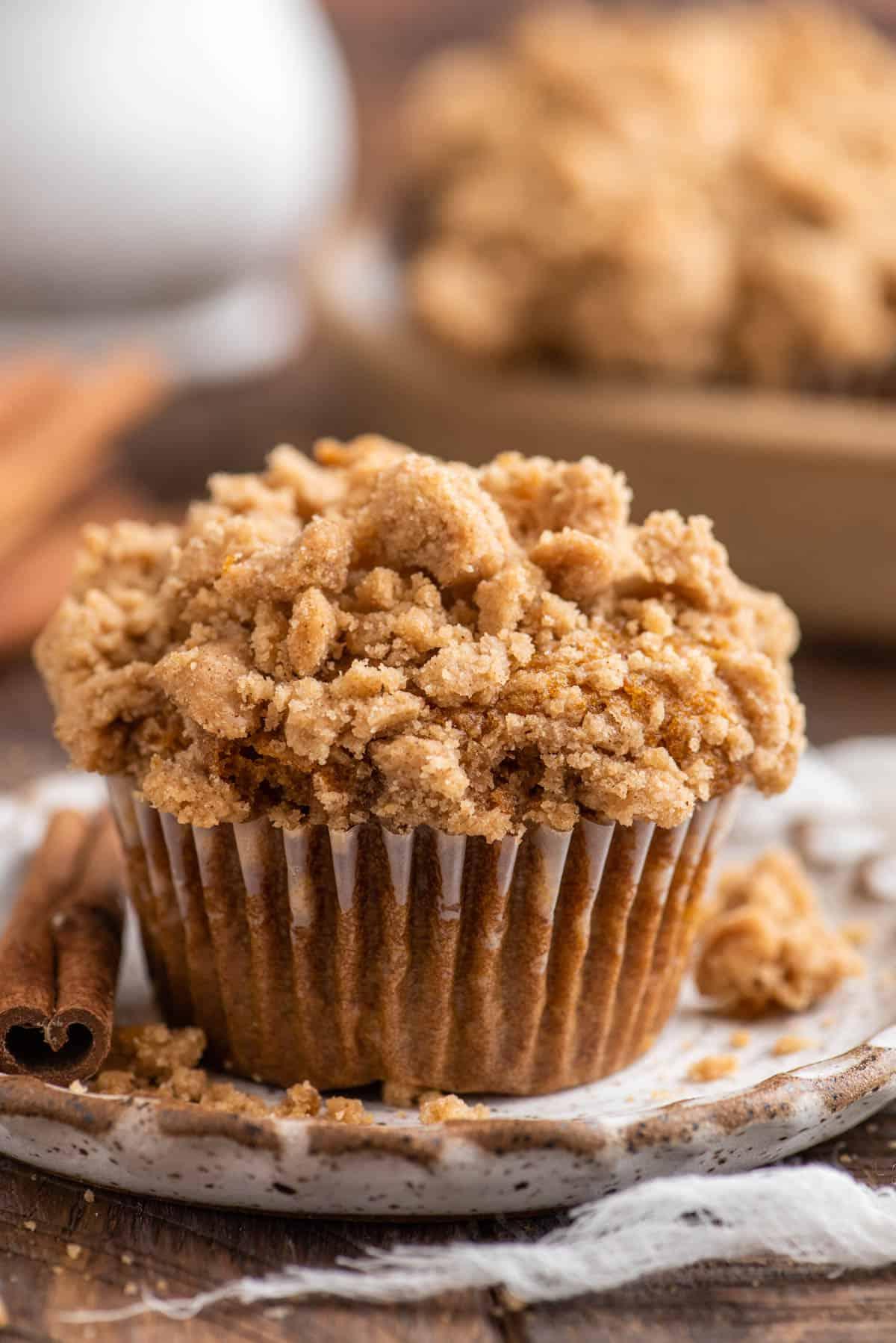 Muffin alla Zucca e Streusel Senza Glutine 11 Muffin singolo di zucca con topping di crumble su un piatto di ceramica maculato su sfondo marrone