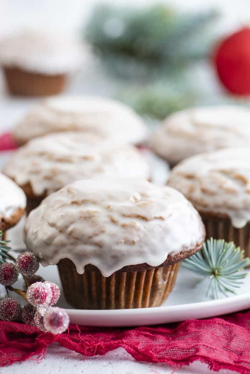 Muffin al pan di zenzero 11 Muffin al pan di zenzero con glassa alla vaniglia disposti su un piatto bianco con bacche rosse zuccherate e rami di abete sempreverdi