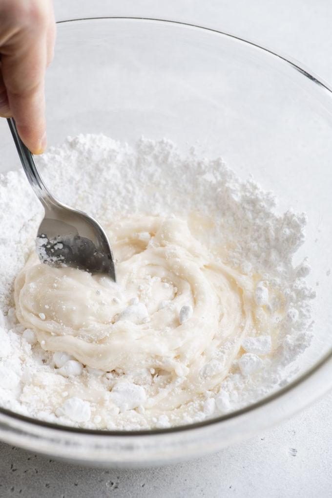 Glassa Reale senza Polvere di Meringa 11 ingredienti per ghiaccia reale mescolati con un cucchiaio in una ciotola di vetro trasparente