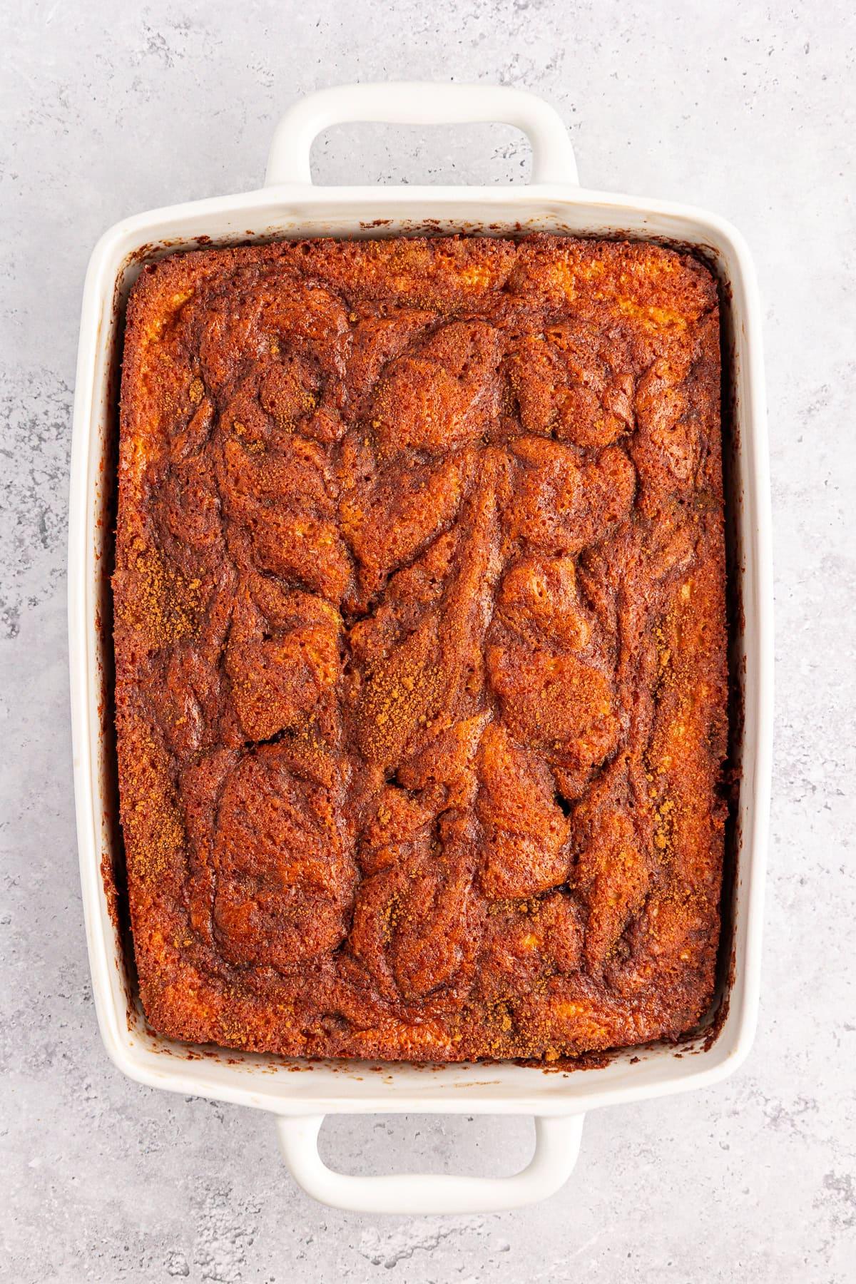 Torta Girella al Miele 11 Una torta Honey Bun con una cima marmorizzata riposa in una teglia rettangolare bianca su uno sfondo grigio chiaro. La delizia di cannella cotta vanta una crosta dorata con spirali più scure, incarnando il perfetto connubio di dolcezza e calore.