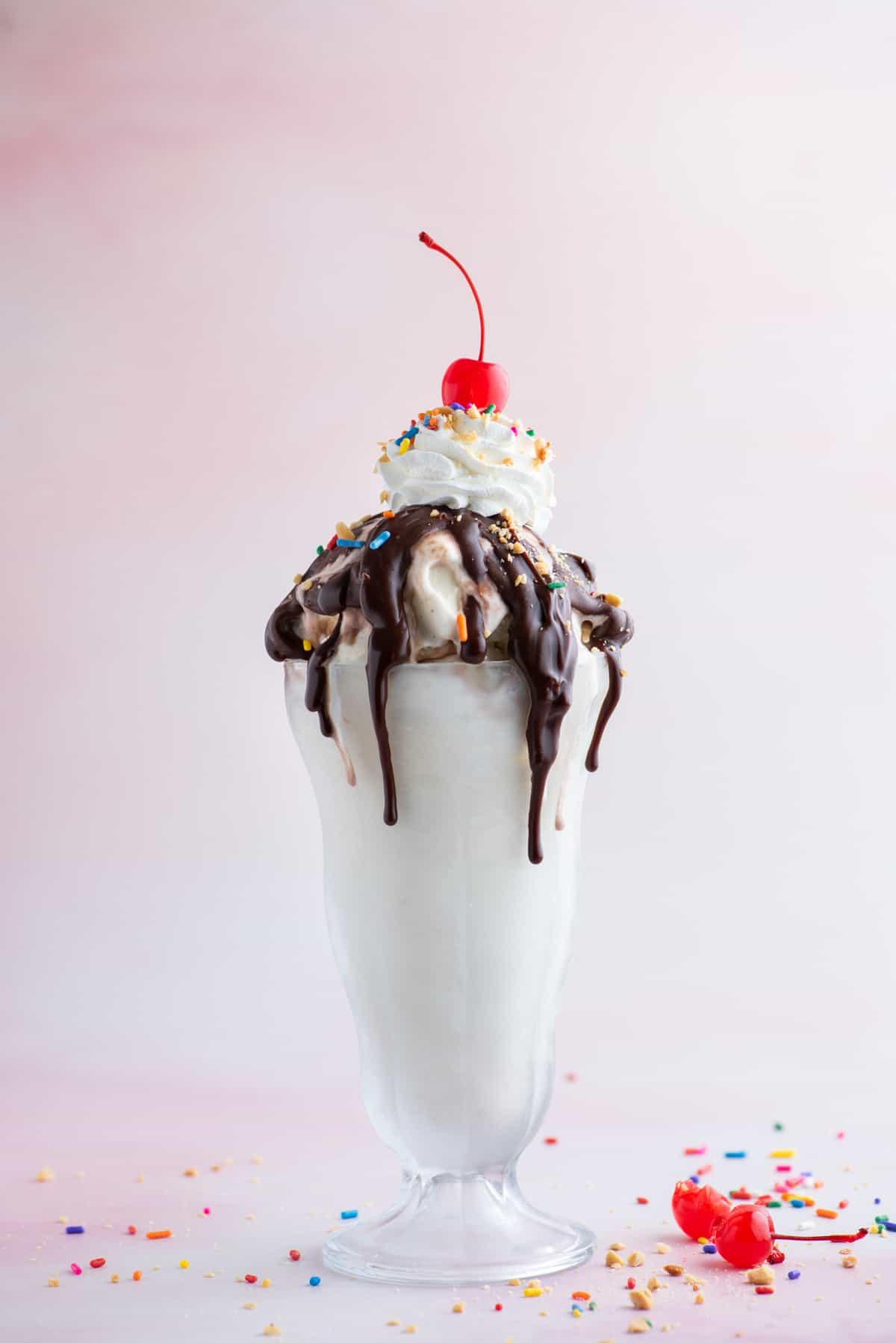 Hot Fudge Sundae 11 Un sundae al cioccolato fuso in un bicchiere alto circondato da codette, pezzi di arachidi e un paio di ciliegie al maraschino