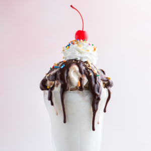 Hot Fudge Sundae 12 Un sundae al cioccolato fuso guarnito con arachidi, codette e una ciliegia, su uno sfondo rosa