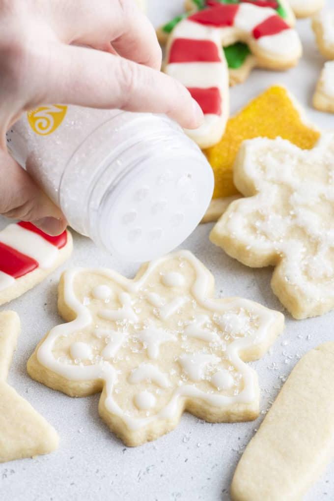 Glassa Reale senza Polvere di Meringa 14 biscotti a fiocco di neve con ghiaccia reale bianca spolverati di zucchero con altri biscotti a tema natalizio sullo sfondo