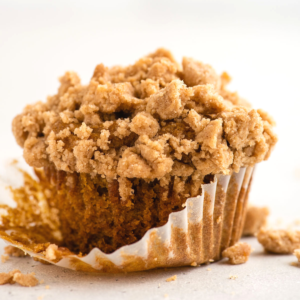 Muffin alla Zucca e Streusel Senza Glutine 14 Primo piano di un muffin di zucca senza glutine con topping di crumble e un pirottino parzialmente rimosso, che mostra una consistenza dorata e umida e il topping sbriciolato.