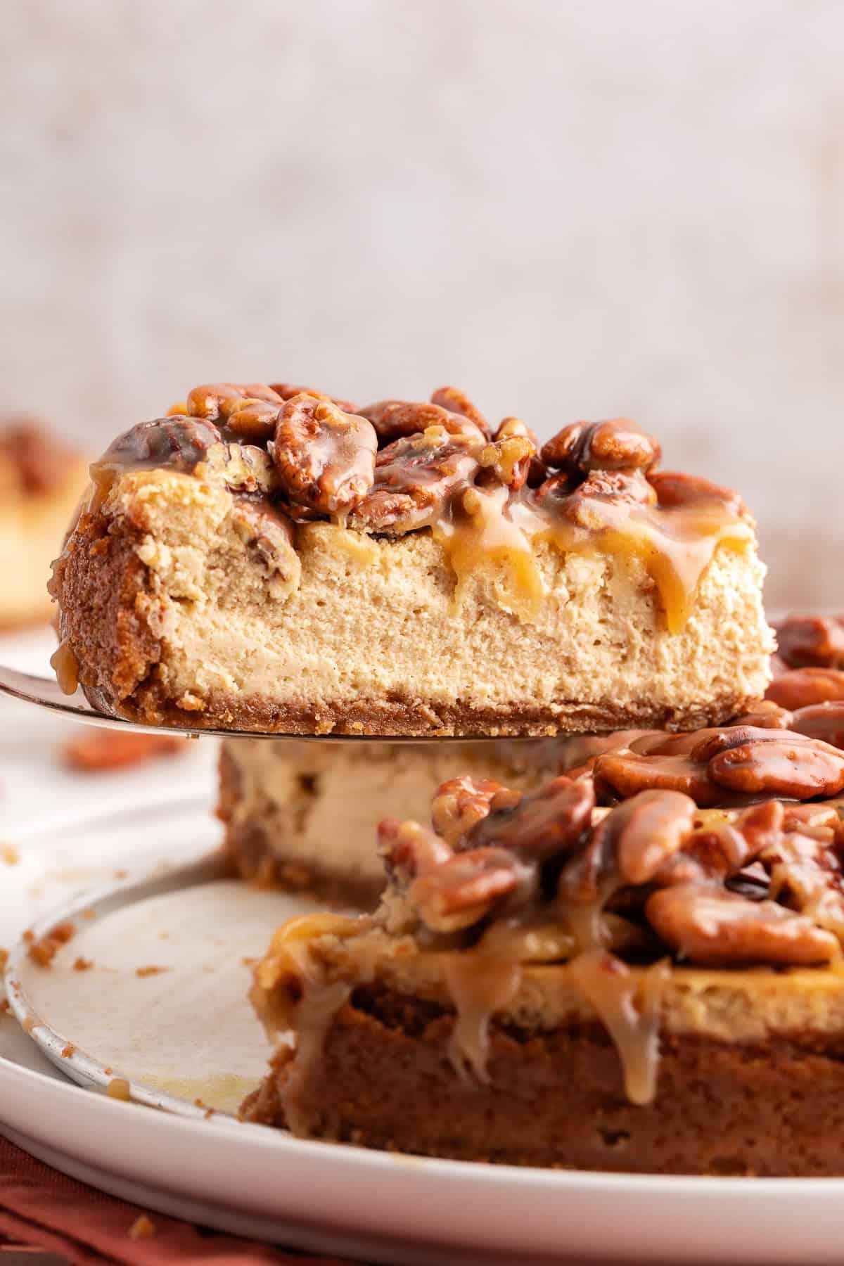 La Migliore Ricetta per Cheesecake alla Torta Pecan 15 Vista laterale di una fetta di cheesecake alle noci pecan sollevata dal resto della cheesecake con una spatola da portata