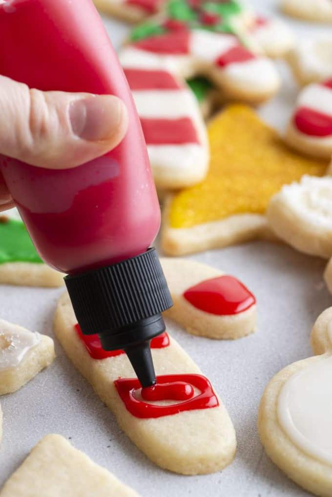 Glassa Reale senza Polvere di Meringa 17 ghiaccia reale rossa applicata su un biscotto a forma di bastoncino di zucchero usando una bottiglia a spremere
