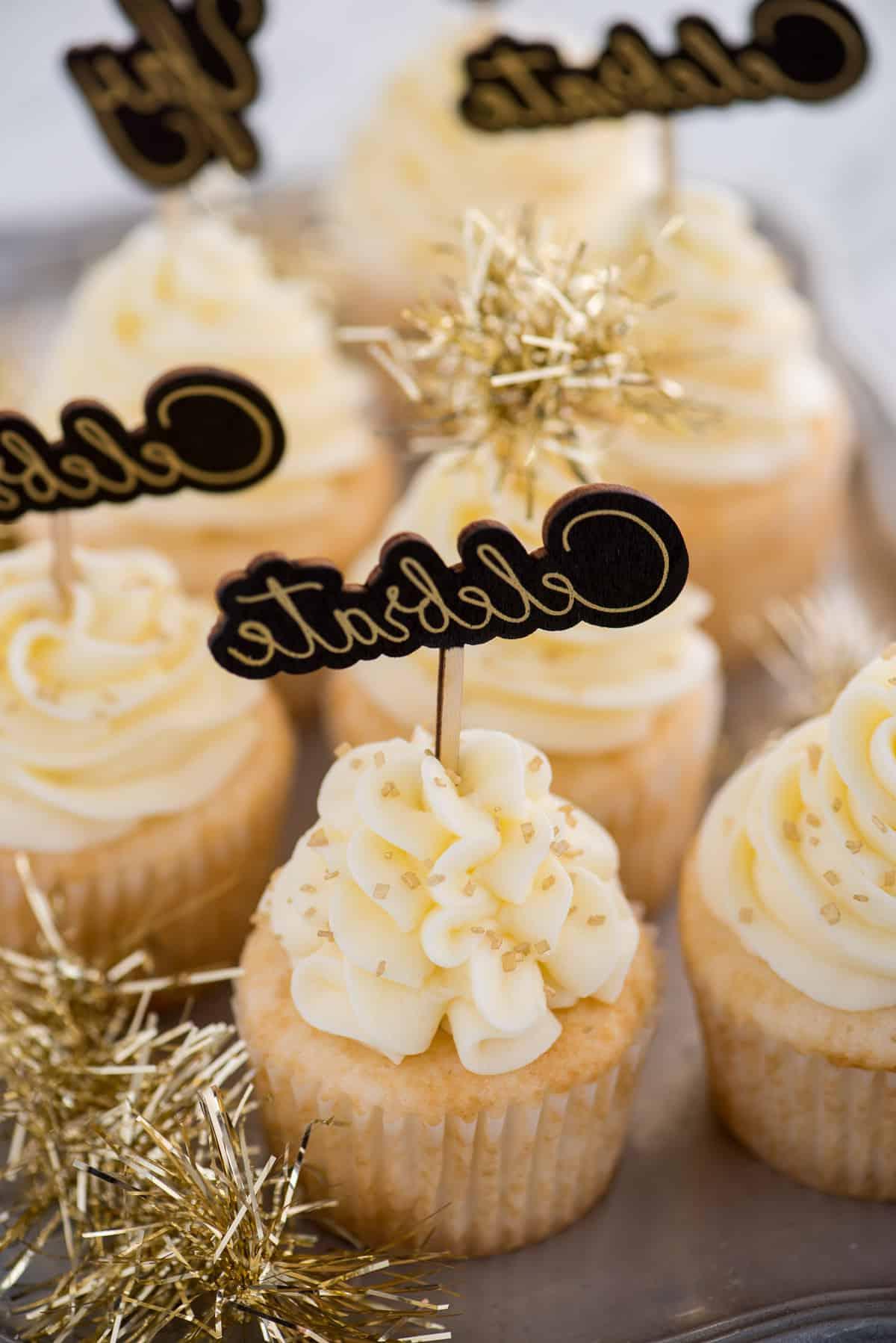 Questa ricetta facile per cupcakes allo champagne con glassa allo champagne è un dessert di Capodanno da non perdere! Come fare i cupcakes allo champagne usando una torta in scatola. Facili cupcakes allo champagne con glassa al burro e champagne, decorati con zuccherini dorati e un topper per cupcake con la scritta "celebrate"
