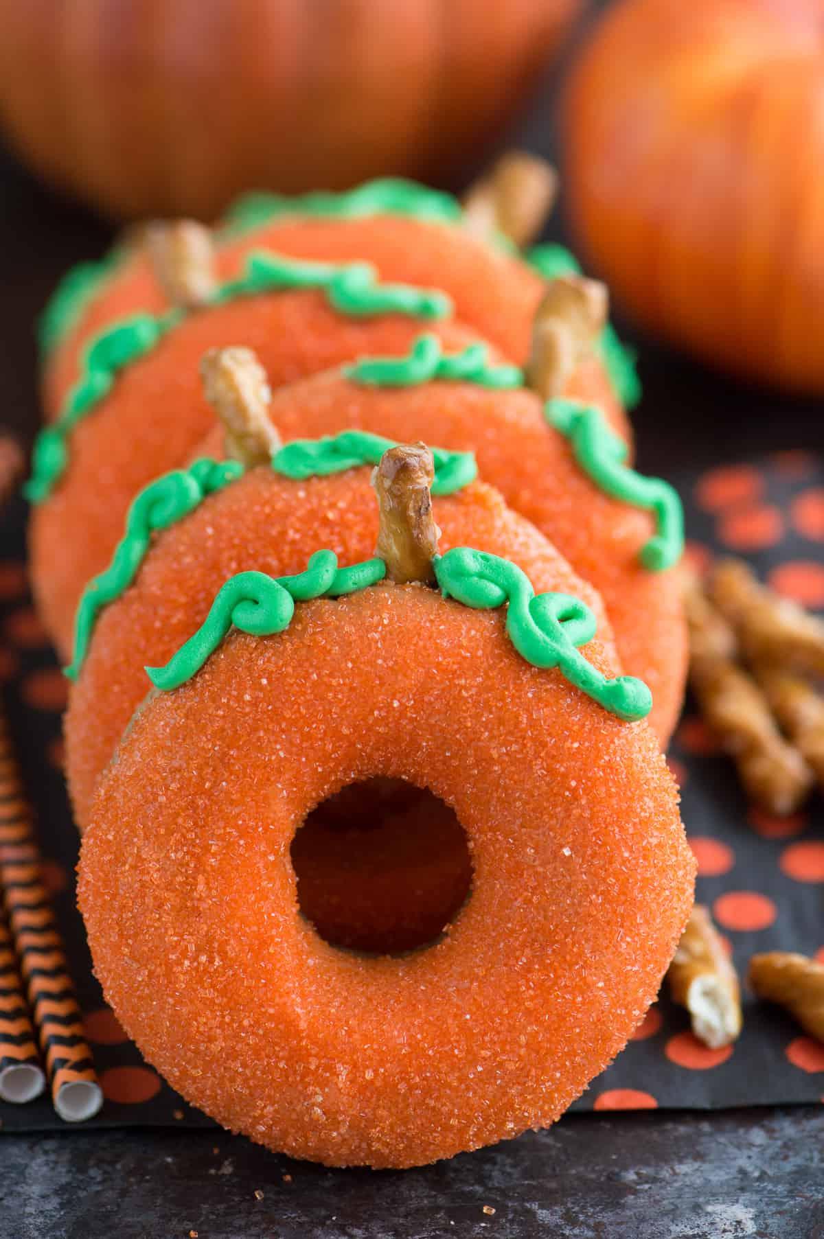 Ciambelle alla Zucca 3 Ciambelle di zucca decorate con glassa arancione, zucchero decorativo e gambo di pretzel, su una griglia di raffreddamento