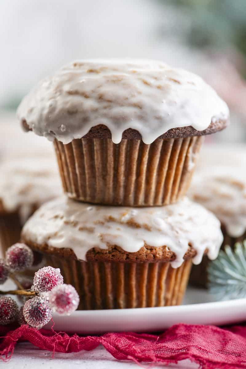 Muffin al pan di zenzero 3 Muffin al pan di zenzero con glassa alla vaniglia disposti su un piatto bianco con bacche rosse zuccherate e rami di abete sempreverdi