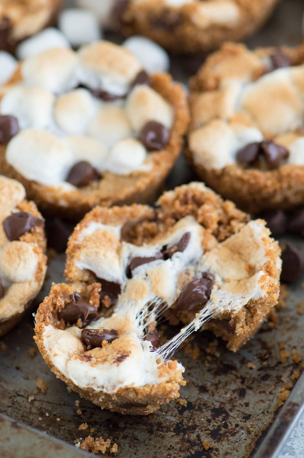 Tazze S'mores al Forno con 5 ingredienti! Preparale in uno stampo per muffin standard. Un incrocio tra biscotti s'mores e cupcake s'mores! Sei Tazze S'mores fatte in casa su una teglia da forno.