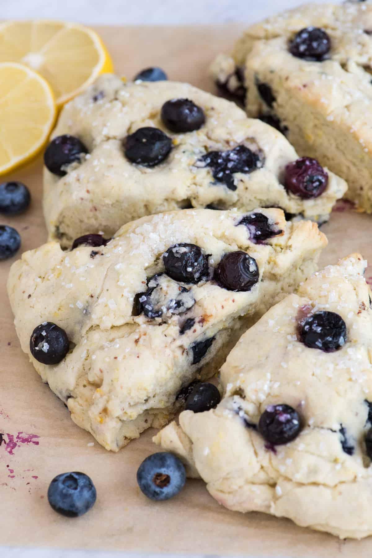 I Migliori Scones al Limone e Mirtilli 4 Scones al limone e mirtilli su carta forno marrone con fette di limone e mirtilli