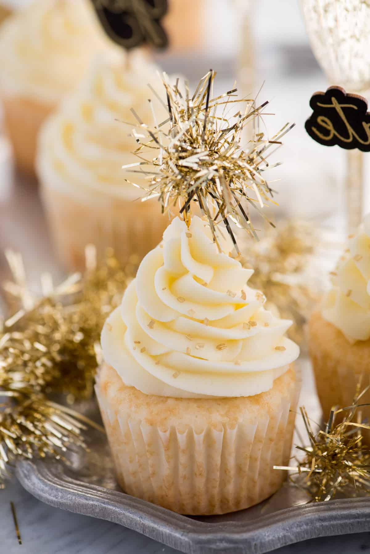 Questa ricetta facile per cupcakes allo champagne con glassa allo champagne è un dessert di Capodanno da non perdere! Come fare i cupcakes allo champagne usando una torta in scatola. Facili cupcakes allo champagne con glassa al burro e champagne, decorati con zuccherini dorati e un topper per cupcake in tinsel dorato