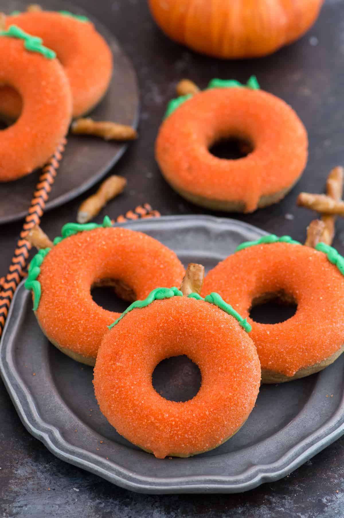 Ciambelle alla Zucca 4 Primo piano di una ciambella di zucca decorata, evidenziando la consistenza morbida, la glassa arancione e il piccolo gambo di pretzel