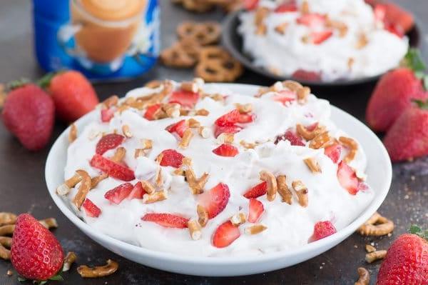 Una ciotola di Insalata Dolce Fragole e Pretzel, con la sua texture morbida e cremosa ben visibile, punteggiata da pezzetti di fragole fresche e pretzel croccanti, pronta per essere gustata.