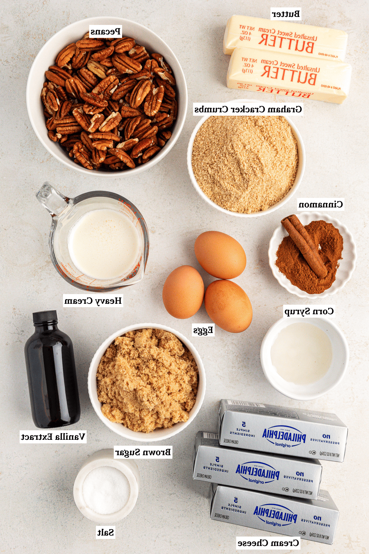La Migliore Ricetta per Cheesecake alla Torta Pecan 4 Vista dall'alto degli ingredienti per la cheesecake alle noci pecan che includono burro, noci pecan, briciole di biscotti graham, cannella, sciroppo di mais, uova, panna fresca, zucchero di canna, estratto di vaniglia e sale