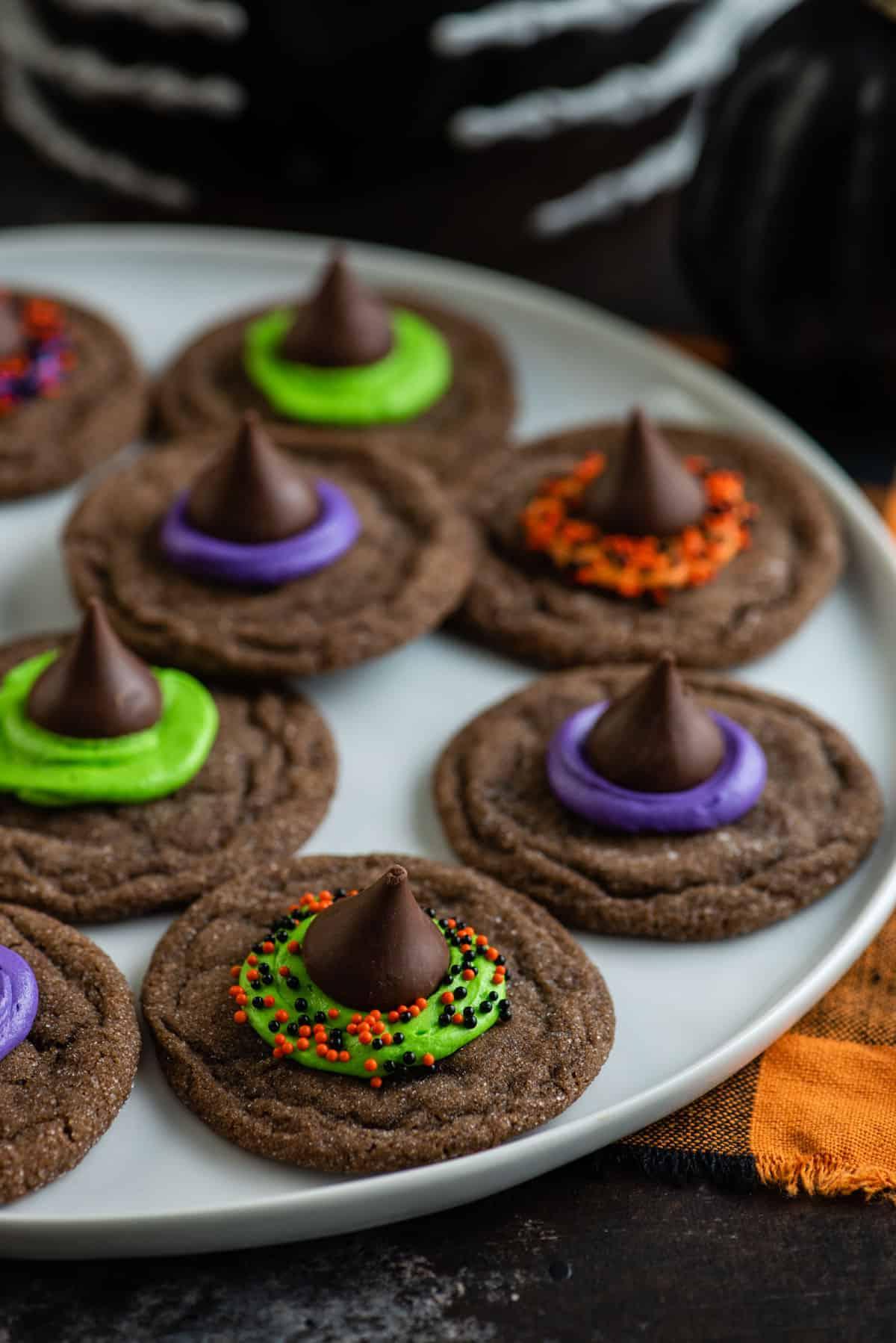Morbidi biscotti al cioccolato sormontati da un bacio di cioccolato, glassa e zuccherini, questi Biscotti Cappello da Strega sono un dessert di Halloween facile. Un piatto di biscotti di Halloween